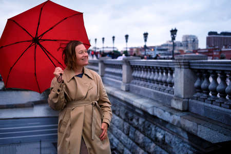 Smiling woman with red umbrella near granite pavement on city streetの写真素材
