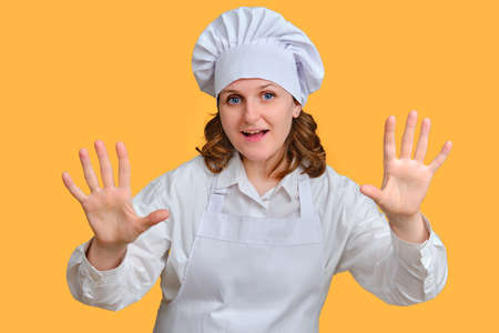 Happy woman chef on yellow studio background shows with hands on copy space for textの写真素材