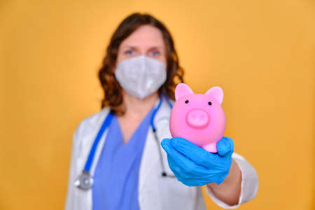 Woman doctor holding piggy bank, yellow studio backgroundの写真素材