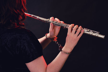 Hands of a woman musician with a flute in handcuffed hands on a black studio background. Problems of...