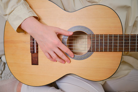 Woman musician playing guitar at home on sofa in living room
