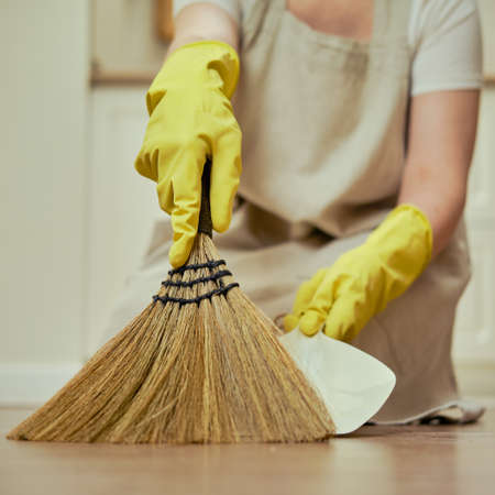 A woman sweeps the floor with a broom when cleaning the home kitchenの写真素材