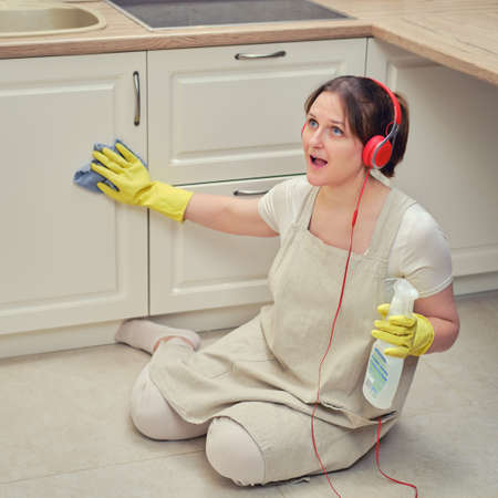 A happy woman with a rag in her hand and headphones sings while cleaning in the home kitchenの写真素材