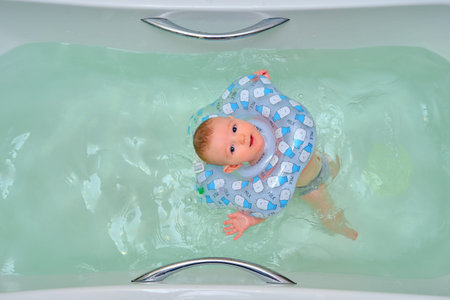 Infant swimming, happy boy swims in a home bath with an inflatable ring on his neck