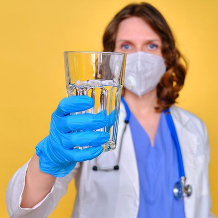 Woman doctor holding a glass of water on a yellow background, close-up.の写真素材