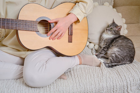 Woman musician playing guitar at home on sofa in living roomの写真素材