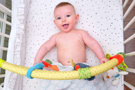 Funny Infant baby playing in the bed with hanging toys, mobile over the cribの写真素材