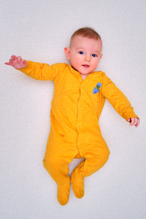 A happy infant baby lying on a play mat in yellow pajamas, top view. Full-length smiling toddler on...