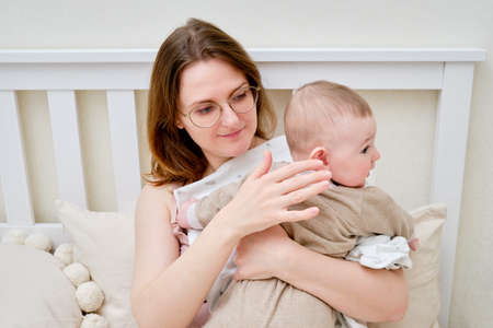 A mother woman holds an infant baby to regurgitate excess air after breastfeeding. Mom with a child boy holds vertically after feedingの写真素材