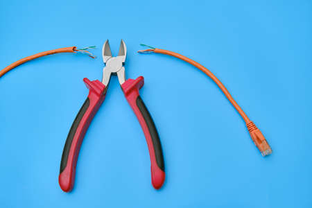 Cutting a computer network wire with wire cutters, blue studio backgroundの写真素材