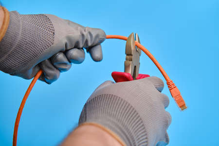 Cutting a computer network wire with wire cutters, blue studio backgroundの写真素材