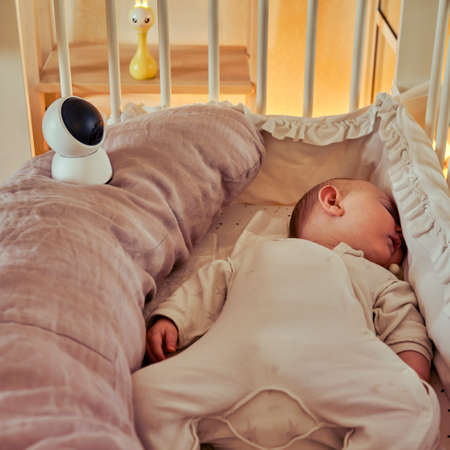 Infant baby sleeps in bed next to home online video cameraの写真素材