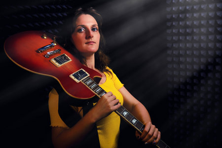 Female guitarist stands with a red electric guitar on his shoulder. A woman in yellow clothes at the recording studio, copy space.の写真素材