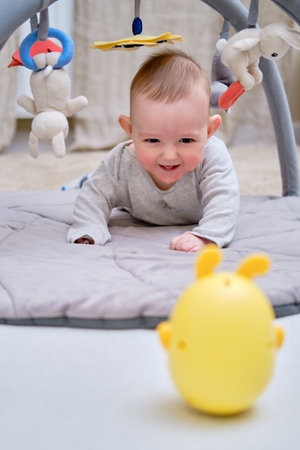 Happy infant baby is playing lying on a mat with toys suspended over itの写真素材
