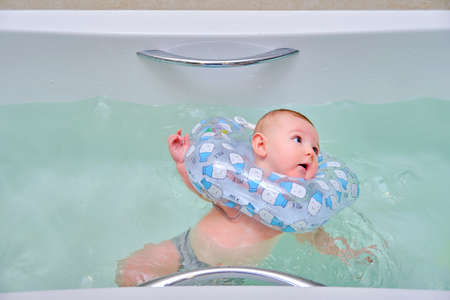 Infant swimming, happy boy swims in a home bath with an inflatable ring on his neckの写真素材
