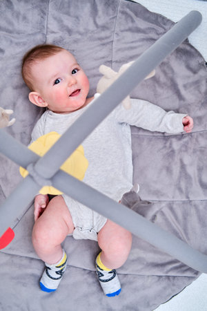 Happy infant baby is playing lying on a mat with toys suspended over it