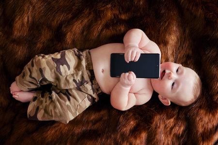 Funny happy baby boy with a phone in his hands on a fur carpet. Smiling child holds a smartphone, top viewの写真素材