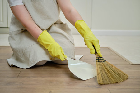 A woman sweeps the floor with a broom when cleaning the home kitchen