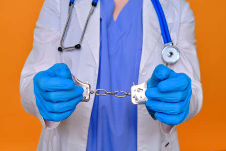 A nurse on a red background shows hands in handcuffs, closeup. Doctor arrested for a bribe from a patient, conceptの写真素材