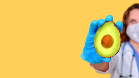 Hand in a medical glove with a avocado vegetable on a yellow background, banner copy spaceの写真素材