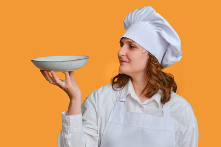 Happy woman chef with empty white plate in hand on studio background, mockup copy space