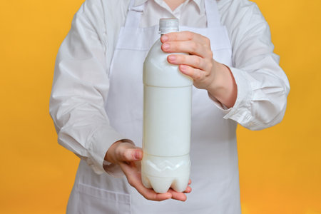 Man chef on a yellow studio background with a plastic bottle of milk in her handsの写真素材
