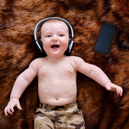 Funny happy baby boy listens to music in wireless headphones online from his phone. Smiling child is...