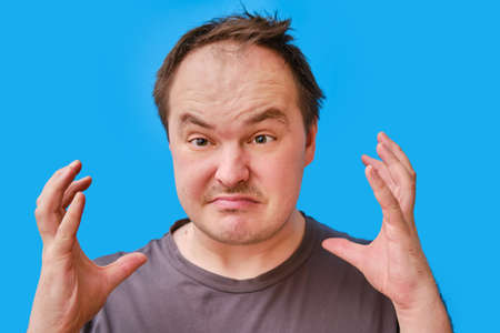 Portrait of an enraged adult man with a disheveled appearance, blue studio backgroundの写真素材