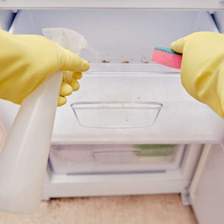 Cleaning the refrigerator freezer from dirt, a man hand in yellow gloves wipes kitchen appliancesの写真素材