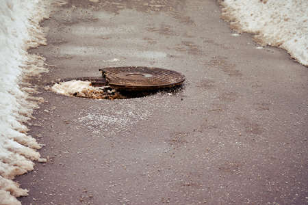 Open broken sewer manhole on winter asphalt roadの写真素材