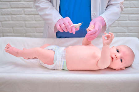 The doctor cuts the nails on the hand of a newborn baby. Nurse in uniform with scissors for child hygieneの写真素材