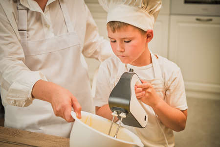 Mother and son cooking apple pie in the home kitchen. A woman and a boy in chef hats and aprons cook with pastriesの写真素材