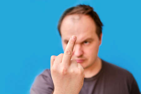 Portrait of disheveled adult man with fucking gesture, blue studio backgroundの写真素材