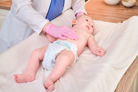 The doctor does gymnastics and massage to a newborn baby. Nurse in uniform doing warm-up exercises...