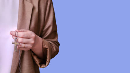 Woman teacher holding religious symbol catholic cross on studio blue background, banner close-upの写真素材