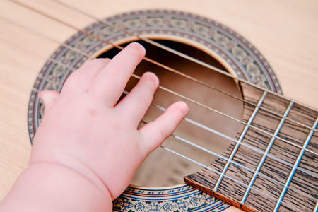 Baby hand and musical instrument guitar, close-up. Children fingers and an object on a white...
