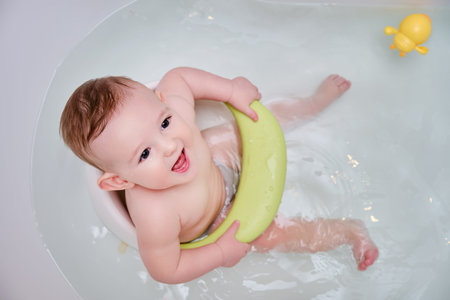 Toddler baby plays with a yellow duck toy while bathing. A happy infant child bathes in water while...