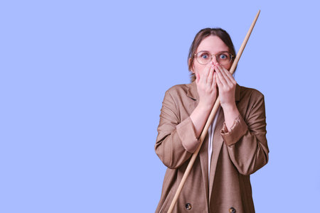 Scared female teacher with pointer on studio blue background, copy space
