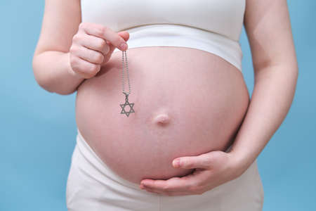 A symbol of the Jewish religion in the hands of a pregnant woman, a studio photo on a blue backgroundの写真素材