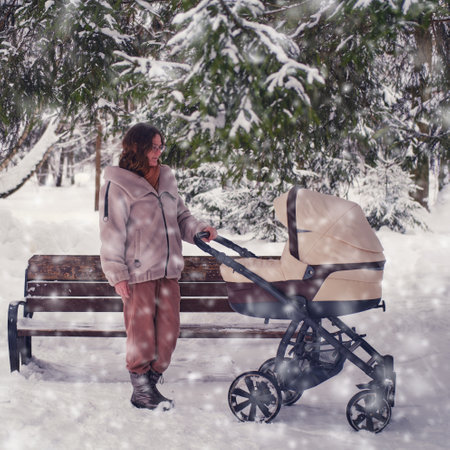 Mom with a baby in a stroller in nature near the trees in the snow. A mother woman with a stroller for a child stands at a bench in a snowy winter parkの写真素材