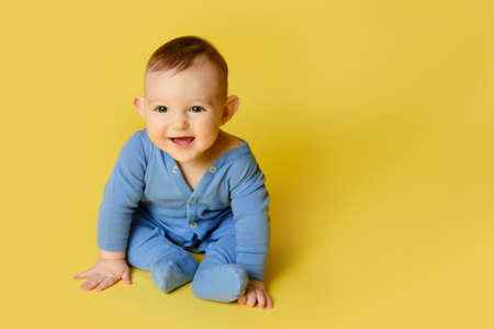 Happy toddler baby plays laughing on studio yellow background. Funny child boy at the age of six months sits and smiling, copy spaceの写真素材