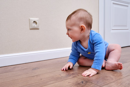 Baby toddler is near the electrical outlet on the home wall. Danger and protection of child fingers...