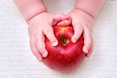Baby hand and red apple fruit, close-up. Children fingers and an object on a white backgroundの写真素材