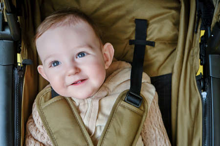 A happy child is sitting in a baby carriage on a studio yellow background. Smiling toddler baby boy in a transformer stroller for transporting children, age eight monthsの写真素材