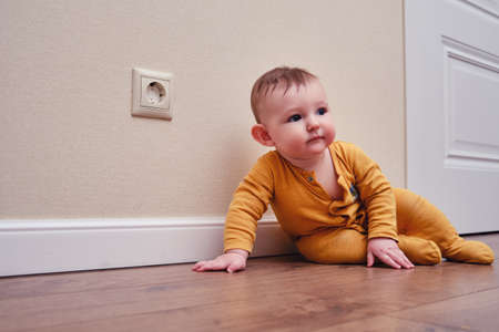 Baby toddler is near the electrical outlet on the home wall. Danger and protection of child fingers from electric shock, aged 6-11 monthsの写真素材
