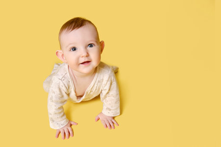 Happy toddler baby crawling on studio yellow background. Funny child boy with a smile on his face,...