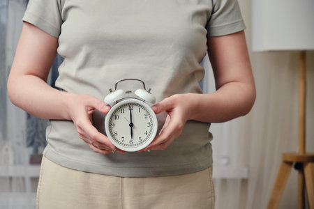 A woman holds a white alarm clock in her hands while standing in a home living room