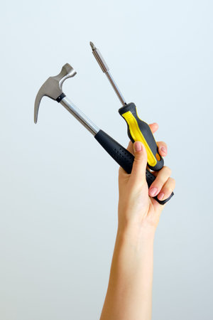 Hammer and screwdriver in hand stretched up on a white background. Outstretched construction toolsの写真素材