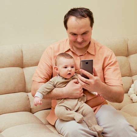 Man father and boy son take selfie photo on phone on sofa in home living roomの写真素材