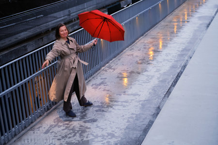 A woman under a red umbrella stands on a city street
